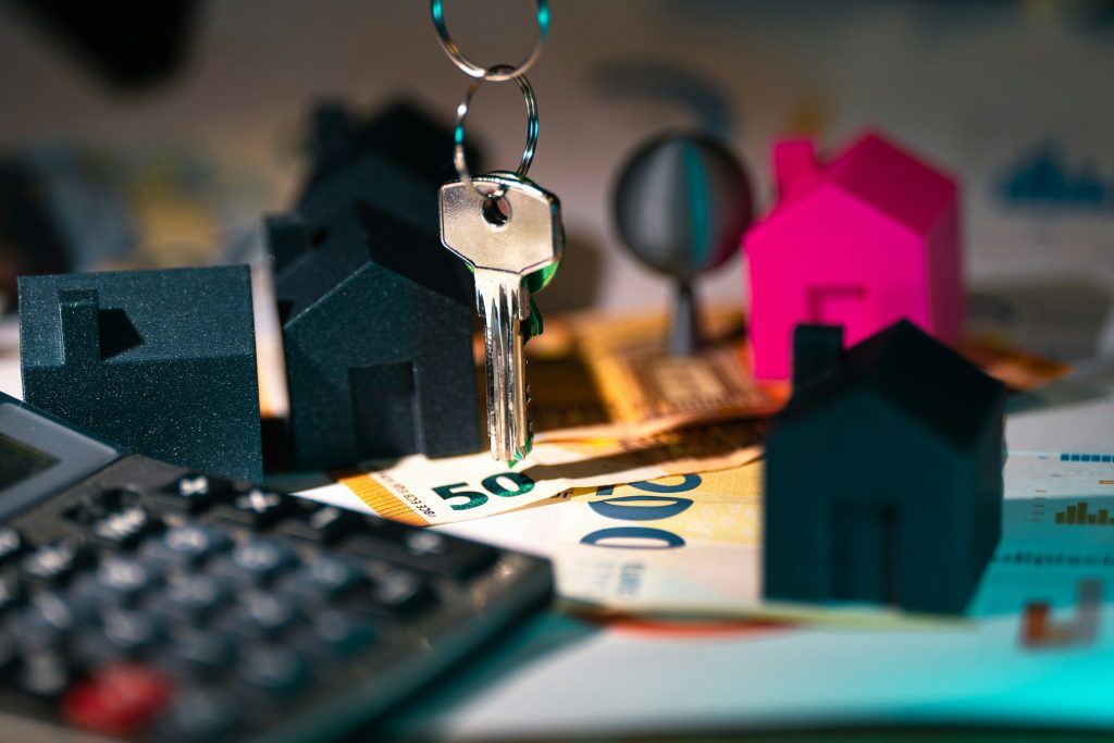 Model houses, a house key, euro banknotes and a calculator on a desk